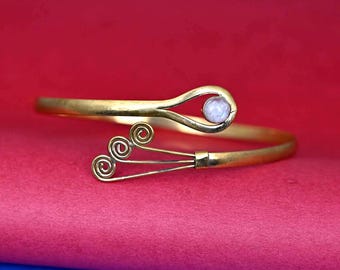May include: A gold-toned bangle bracelet with a white pearl-like stone and a decorative swirl design.