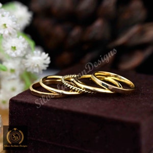 Könnte beinhalten: Satz von vier goldfarbenen Stapelringen. Die Ringe haben unterschiedliche Breiten und Stile, darunter ein gedrehtes Band.