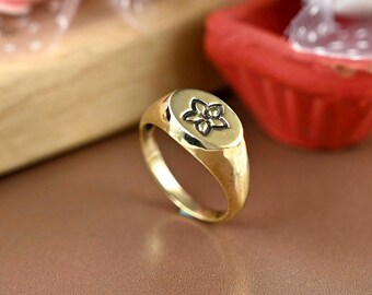 Könnte beinhalten: Ein goldener Siegelring mit einem Blumendesign auf der Oberseite. Der Ring ist oval geformt und hat eine glatte, polierte Oberfläche.