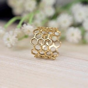 May include: A gold honeycomb ring with a textured design. The ring is made of metal and has a shiny finish.