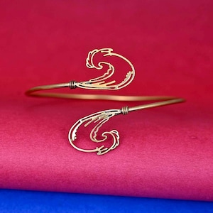 May include: A gold-toned metal bracelet with a wave design. The bracelet is open and has a simple, minimalist style.