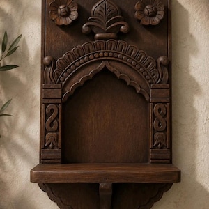Könnte beinhalten: Ein dunkelbraunes Wandregal aus Holz mit einem gewölbten Nischendesign. Die Rückwand ist aufwendig mit Blumenmotiven in den oberen Ecken, einem zentralen Spitzbogen und geometrischen Mustern entlang der vertikalen Seitensäulen verziert.