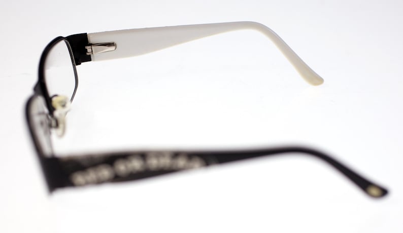 May include: Black-framed spectacles with white arms. The glasses have a black frame around the lenses and white arms that curve to the ears. The background is white.