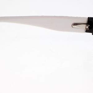 May include: Black and white spectacles with a rectangular frame. The arms are white, and the frame is black. The glasses are designed for vision correction and are suitable for daily wear.