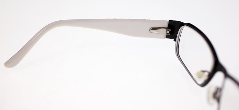May include: Black and white spectacles with a rectangular frame. The arms are white, and the frame is black. The glasses are designed for vision correction and are suitable for daily wear.