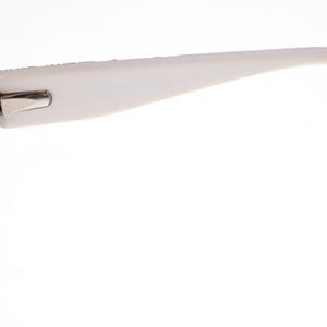 May include: Close-up of eyeglasses with a black frame and white temples. The glasses have a rectangular lens shape and a silver hinge. The white temples curve gently, ending in a rounded tip. The background is plain white.