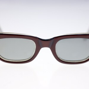 Op de afbeelding: Een paar vintage bruine plastic zonnebrillen met zilveren accenten en een vlinderontwerp aan elke kant van het montuur.