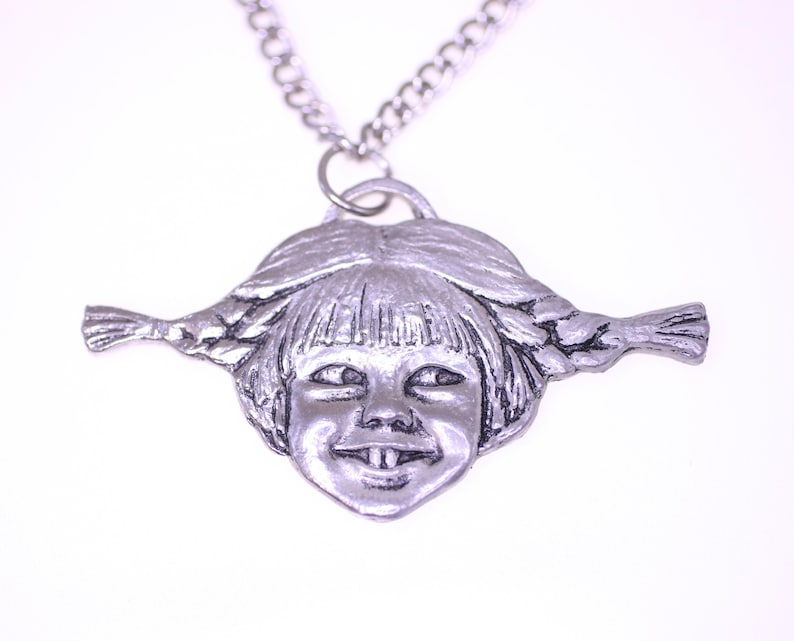 May include: Silver-toned pendant necklace featuring a smiling face with pigtails. The pendant is a detailed, three-dimensional design of a child's face with a wide grin and braided hair, suspended from a silver chain.