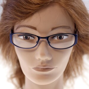 May include: A close-up of a mannequin wearing blue-framed spectacles. The spectacles have a rectangular shape with rounded edges. The mannequin has brown hair and a neutral expression.
