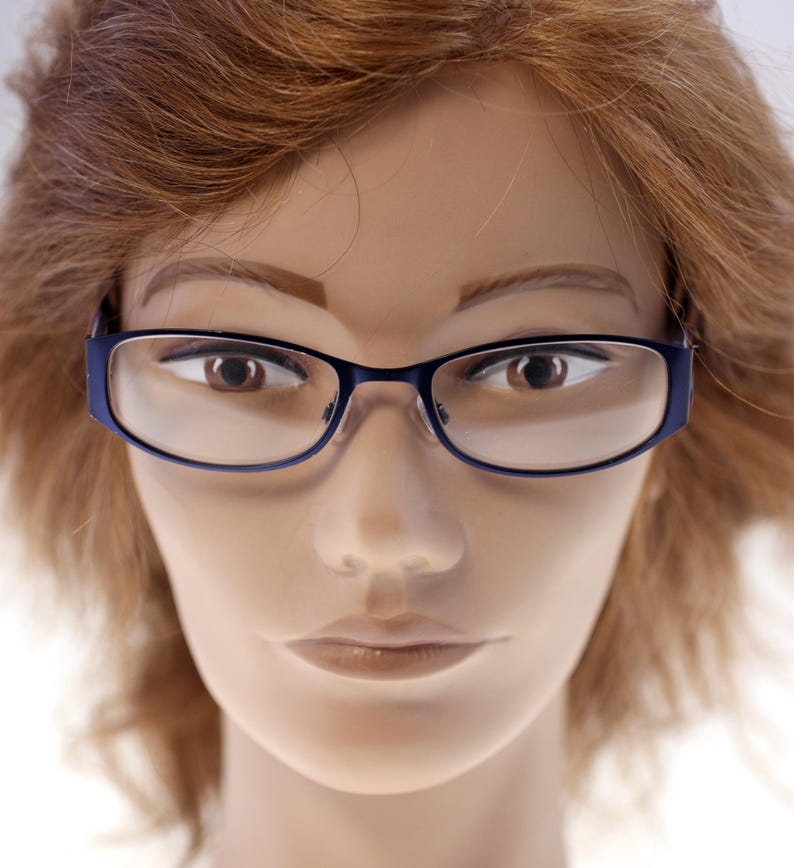 May include: A close-up of a mannequin wearing blue-framed spectacles. The spectacles have a rectangular shape with rounded edges. The mannequin has brown hair and a neutral expression.