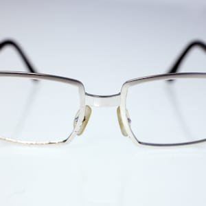 Könnte beinhalten: Silberfarbene rechteckige Brille mit dünnem Metallrahmen.