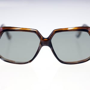 Puede incluir: Gafas de sol geométricas en tonos marrón y beige con montura octogonal. Lentes grises. Pequeños detalles plateados en las esquinas de la montura. Estilo retro.