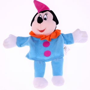 Könnte beinhalten: Eine blaue und orangefarbene Plüschpuppe von Mickey Mouse, die als Clown verkleidet ist. Die Puppe hat einen rosa Hut, eine rosa Nase und rosa Knöpfe auf ihrem blauen Hemd. Die Puppe hält ihre Arme seitlich ausgestreckt.