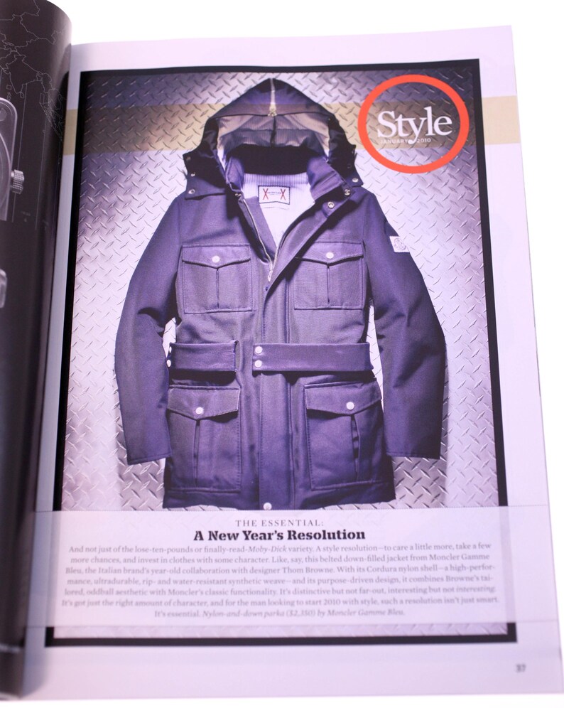 Puede incluir: Una chaqueta con capucha azul marino oscuro con m&uacute;ltiples bolsillos delanteros y un cintur&oacute;n. La chaqueta aparece en una revista con la palabra "Style" en un c&iacute;rculo rojo. Tambi&eacute;n se ve el texto "A New Year's Resolution".