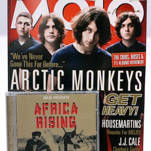 May include: A magazine cover featuring a photo of the band Arctic Monkeys with the title "Arctic Monkeys" in large, bold letters. The cover also features a smaller image of a CD with the title "Africa Rising" and the text "Mojo Presents".