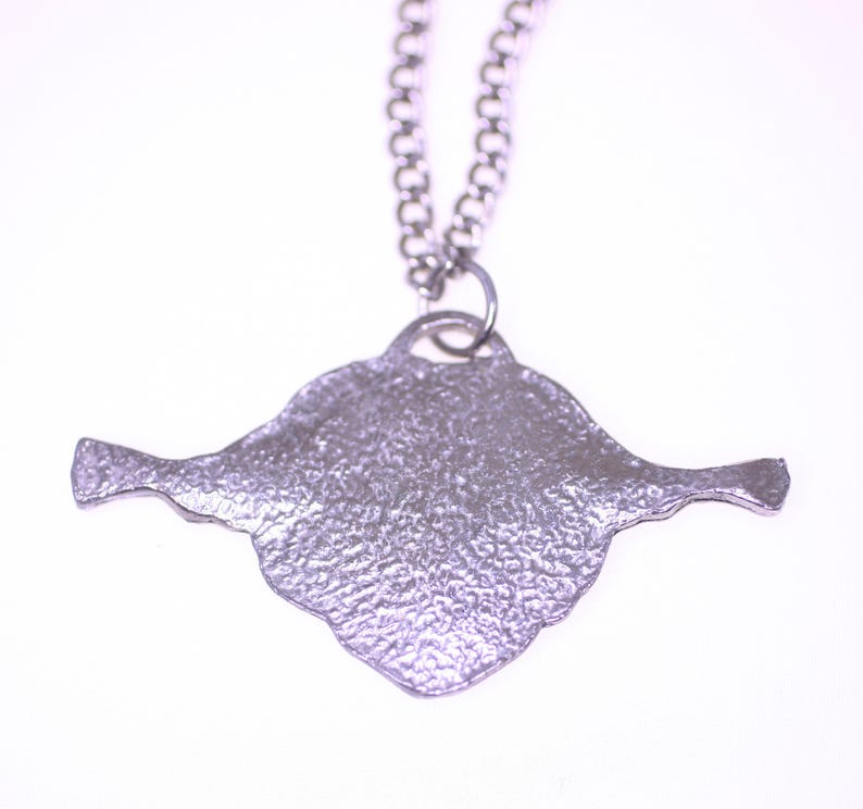 May include: A silver-colored pendant necklace. The pendant has a textured, irregular shape with two extended wing-like features. The chain is a delicate, linked design. The necklace is set against a white background.
