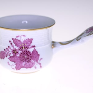 May include: A white porcelain creamer with a pink floral design and a gold rim. The creamer has a handle that is shaped like a swan's neck.