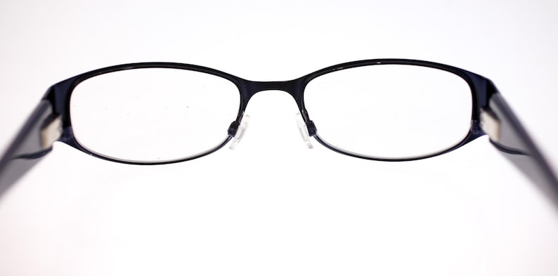 May include: Black-framed spectacles with oval lenses. The glasses have a thin frame and nose pads. The temples are dark and extend to the sides. The background is white.