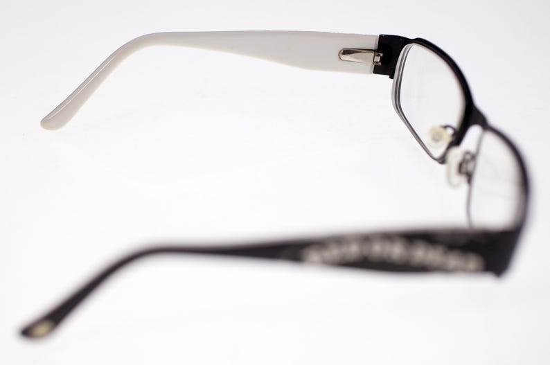 May include: Black and white spectacles with a rectangular frame and clear lenses. The arms are white, and the frame is black with decorative detailing. The glasses are designed for vision correction.