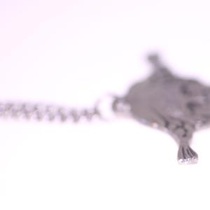 May include: A silver-toned pendant necklace featuring a detailed, textured manta ray design. The pendant is suspended from a delicate chain, creating a minimalist and elegant aesthetic. The necklace is set against a bright white background.