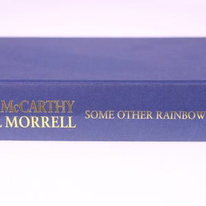 May include: A hardcover book titled "Some Other Rainbow" by John McCarthy & Jill Morrell. The book has a deep blue cover with gold lettering. The Bantam Press logo is visible on the spine.