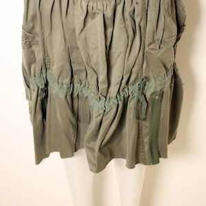 May include: A green, gathered skirt with a zipper and a tie detail. The skirt has a ruffled hem and pockets on the sides.