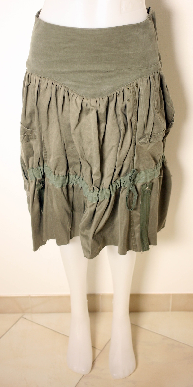 May include: A green, gathered skirt with a zipper and a tie detail. The skirt has a ruffled hem and pockets on the sides.