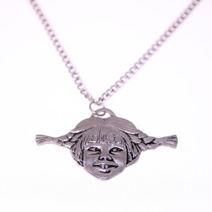 May include: A silver-toned pendant necklace featuring a detailed face with braided pigtails. The pendant is a sculpted design of a smiling girl's face. The necklace chain is a simple, linked design.