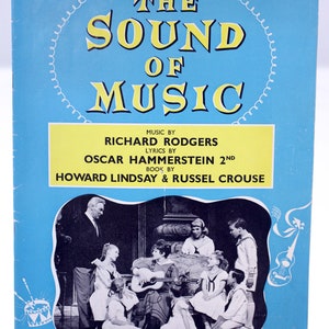 Könnte beinhalten: Ein blaues und weißes Programm für das Musical "The Sound of Music" im Palace Theatre in London. Das Programm zeigt ein Schwarzweißfoto der Besetzung, die auf der Bühne spielt. Der Text auf dem Programm enthält die Namen der Komponisten, Texter und Buchautoren.