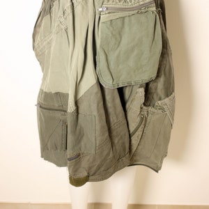 May include: A green utility skirt with multiple pockets and a zippered pocket on the right side. The skirt is made of a patchwork of different fabrics and has a frayed hem.