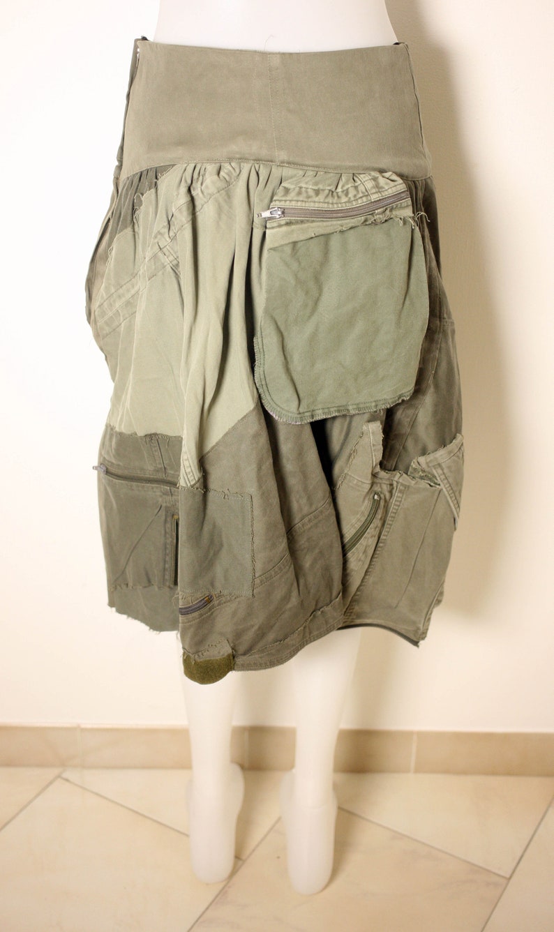 May include: A green utility skirt with multiple pockets and a zippered pocket on the right side. The skirt is made of a patchwork of different fabrics and has a frayed hem.
