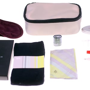 May include: A collection of travel accessories, including a beige cosmetic bag with a black trim, a burgundy eye mask, and a black box with the text "SPACE NK". Also included are a small mirror, a toothbrush, toothpaste, and a pen.