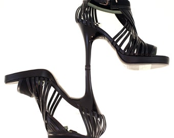 May include: A pair of black high-heeled sandals with a strappy design. The sandals have a thin stiletto heel and a platform sole.
