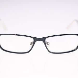 May include: Rectangular eyeglasses with black frames and clear lenses. The temples are a light colour. The glasses are displayed against a white background.