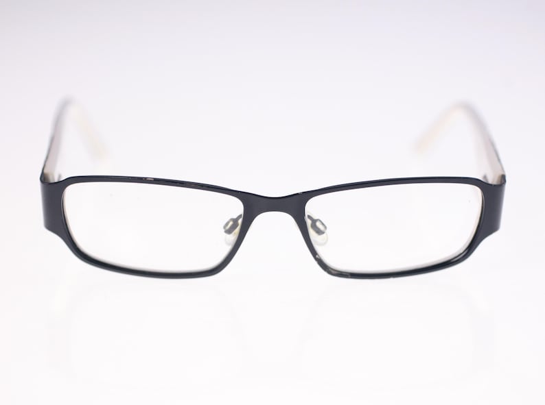 May include: Rectangular eyeglasses with black frames and clear lenses. The temples are a light colour. The glasses are displayed against a white background.