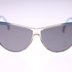 May include: Vintage sunglasses with a light blue frame and gray lenses. The sunglasses have a unique, curved design. The frame is a translucent light blue color, and the lenses are a solid gray. The overall style is retro.