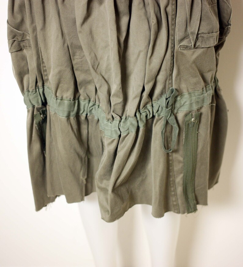 May include: A green utility skirt with a drawstring waist and a zipper on the side. The skirt is made of a durable, lightweight fabric.