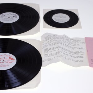 Peut inclure: Un ensemble de quatre disques vinyles, dont deux grands disques noirs avec des pochettes en papier blanc, un disque noir plus petit avec une pochette en papier blanc et une feuille de papier blanc avec du texte. Les disques les plus grands ont un texte rouge qui dit "The Rhythm Method of Modern Percussion - Advanced Course".