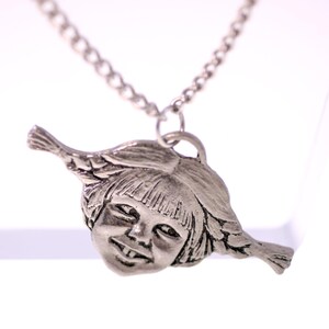 May include: A silver-toned pendant necklace featuring a detailed, smiling face with bangs and side braids. The pendant is suspended from a delicate chain. The necklace is displayed against a bright white background.