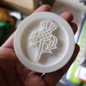 May include: White plastic cookie cutter shaped like a stylized thistle flower.