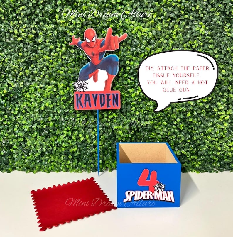 May include: A blue and red cardboard box with a Spider-Man design and the number 4. The box is decorated with a spider web and the words "Spider-Man". The box is sitting on a green surface. A red felt square is in the lower left corner of the image. A red and blue cardboard cutout of Spider-Man is in the upper left corner of the image. The cutout has the name "Kayden" written on it. A speech bubble with the text "DIY, attach the paper tissue yourself. You will need a hot glue gun" is in the upper right corner of the image.