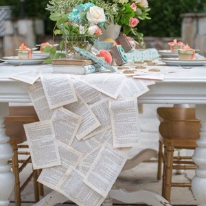May include: A white table with a book page runner. The table is set with a floral centerpiece, peach, and other decorative items. The table is surrounded by chairs.