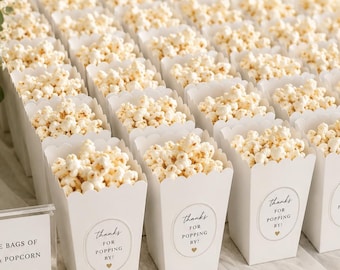 May include: Rows of white popcorn containers filled with popcorn, each featuring a circular sticker that reads 'thanks FOR POPPING BY!'. A sign in a gold frame reads 'A sweet THANK YOU FOR CELEBRATING WITH US!' and another sign reads 'LITTLE BAGS OF LOVE & POPCORN ENJOY!'.