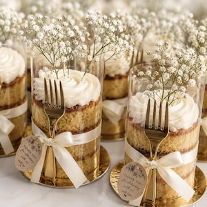 May include: Individual layered cakes in clear cylindrical containers, topped with white frosting and baby's breath flowers. Each cake features a gold fork tied with a cream ribbon and a brown tag reading Thank you for celebrating with us.
