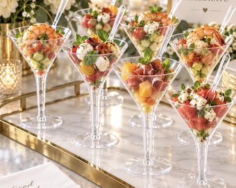May include: A collection of clear plastic martini glasses filled with various appetizers, including shrimp, mozzarella, melon, and watermelon, arranged on a gold-rimmed tray with napkins printed with Good Food Brighter Company and signs.