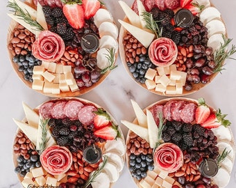 Puede incluir: Cuatro tablas circulares de madera con una variedad de aperitivos dispuestos sobre ellas. Cada tabla presenta una combinación diferente de carnes, quesos, frutas, nueces y otros aperitivos. Las tablas están dispuestas en un patrón cuadrado sobre una superficie blanca.
