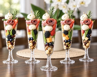 Könnte beinhalten: Fünf durchsichtige Sektgläser aus Kunststoff, gefüllt mit geschichteten Häppchen aus Mozzarellakugeln, gerollter Salami, Erdbeeren, Brombeeren, Blaubeeren, Cheddar-Würfeln, Nüssen und Zweigen aus frischem grünem Rosmarin.