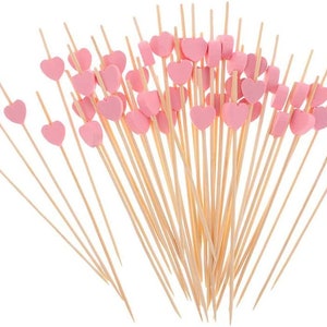 Puede incluir: Un montón de pinchos de madera con tapas en forma de corazón rosa. Los pinchos están dispuestos en forma de abanico.