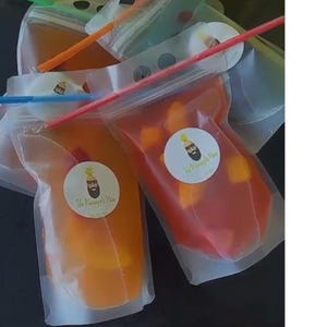May include: Four clear plastic pouches with colourful straws and a logo that says "The Pineapple Man". The pouches contain a red and orange liquid with fruit pieces inside.