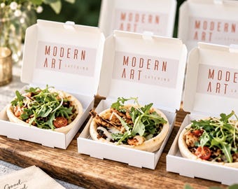 May include: Three individual white cardboard boxes, each containing a small round flatbread topped with grilled chicken, fresh arugula, and sliced cherry tomatoes. The inside lid of each box features the text Modern Art Catering in red.